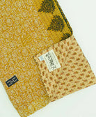 yellow-green floral kantha quilt throw with a tag featuring the hand-stitched signature of the maker