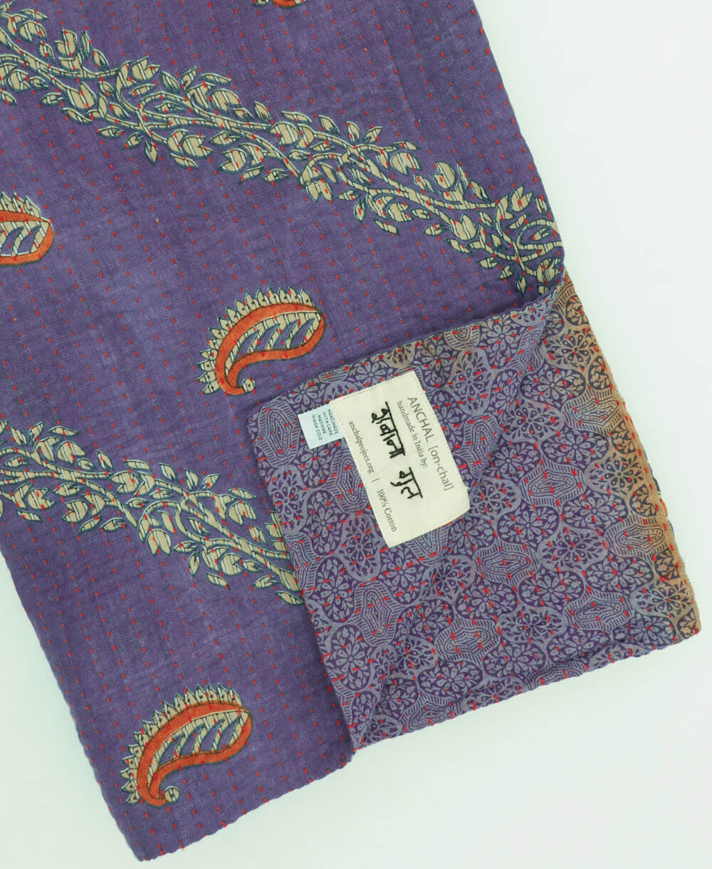 amethyst purple paisley kantha quilt throw with a tag featuring the hand-stitched signature of the maker