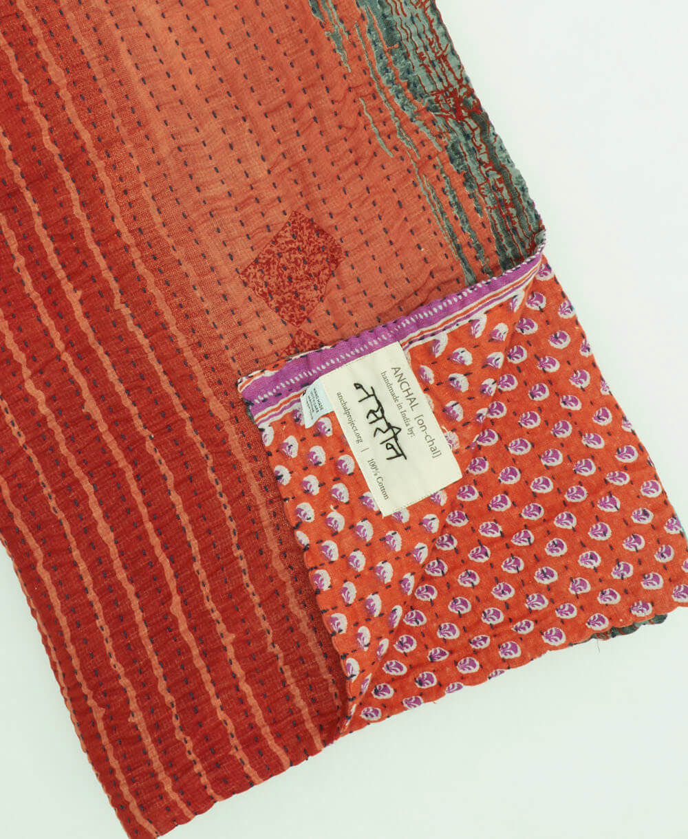 red & coral stripe kantha quilt throw with a tag featuring the hand-stitched signature of the maker