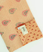 tan paisley kantha quilt throw with a tag featuring the hand-stitched signature of the maker