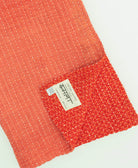 two-tone coral kantha quilt throw with a tag featuring the hand-stitched signature of the maker