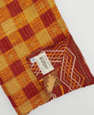 crimson & tan gingham kantha quilt throw with a tag featuring the hand-stitched signature of the maker
