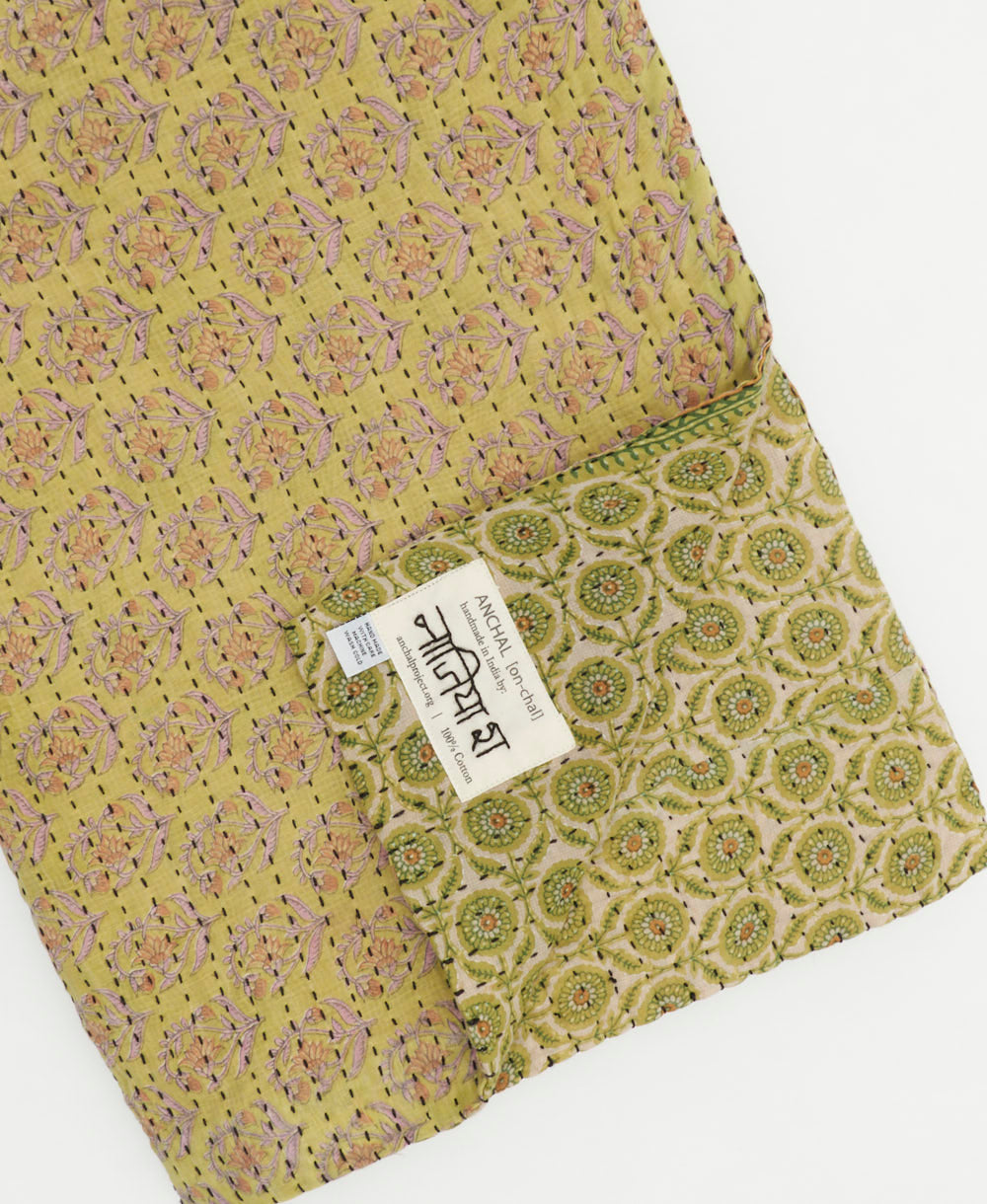 Sage green kantha quilt throw with a tag featuring the hand-stitched signature of the maker