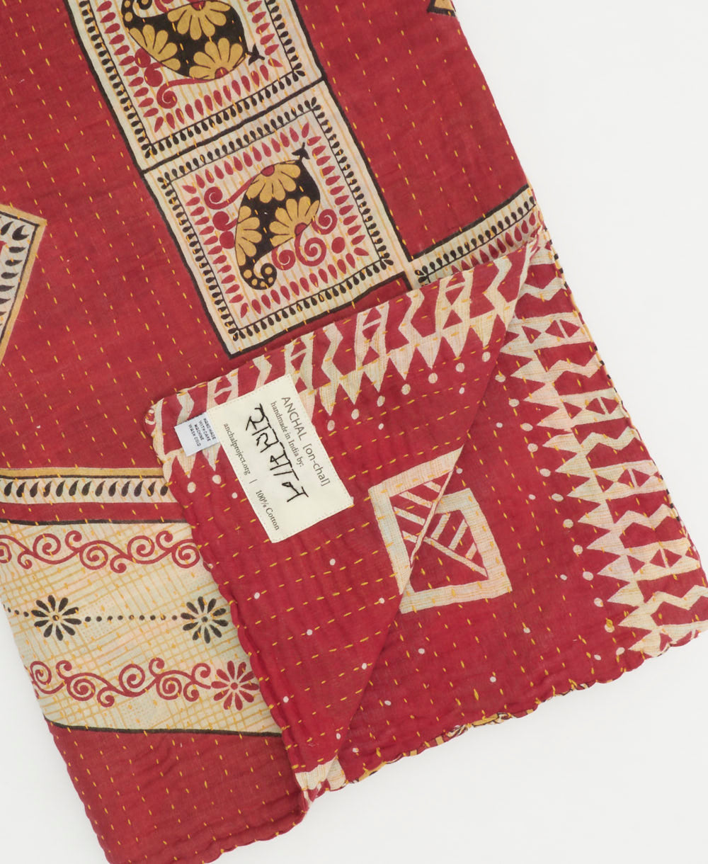 crimson red geometric kantha quilt throw with a tag featuring the hand-stitched signature of the maker