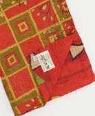 bright red geometric kantha quilt throw with a tag featuring the hand-stitched signature of the maker