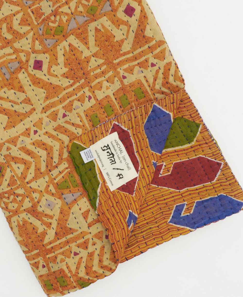 light orange geometric kantha quilt throw with a tag featuring the hand-stitched signature of the maker