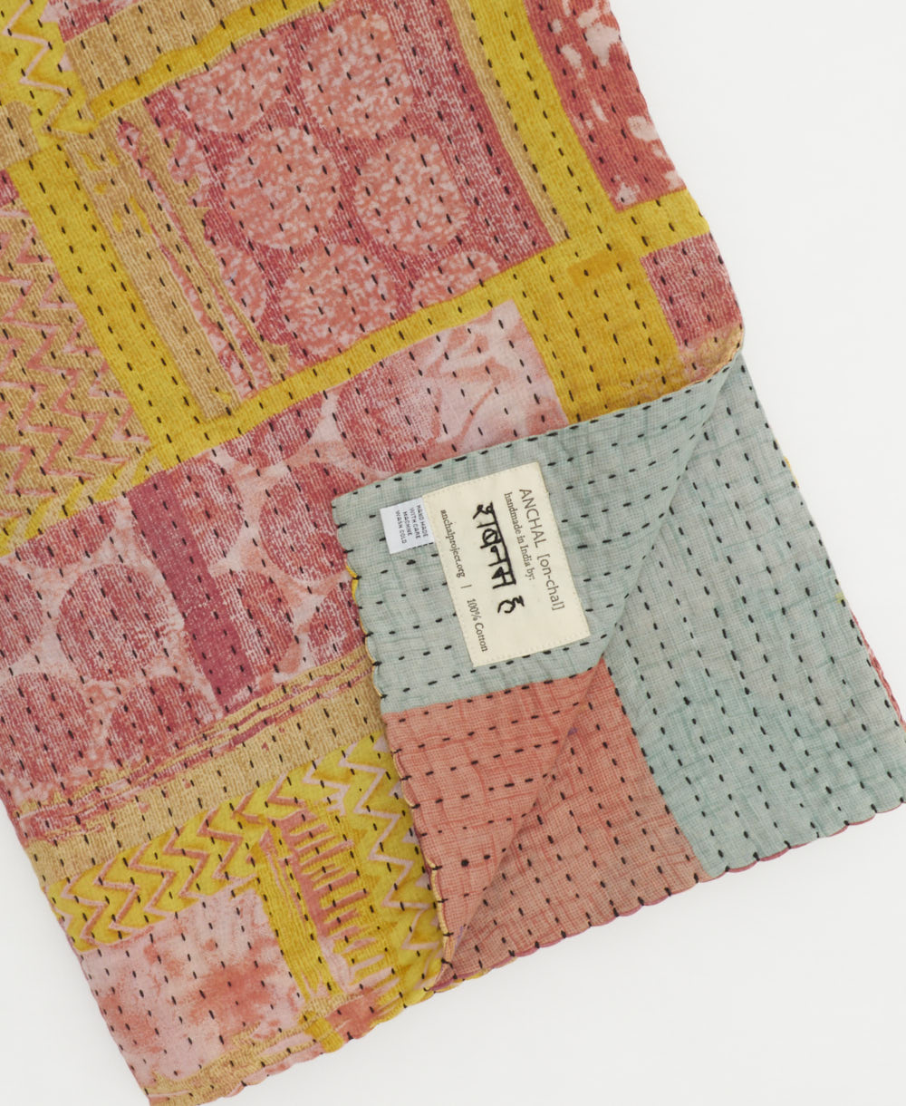 pastel pink geometric kantha quilt throw with a tag featuring the hand-stitched signature of the maker