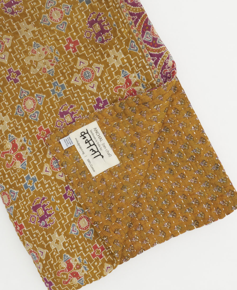 dark mustard kantha quilt throw with a tag featuring the hand-stitched signature of the maker