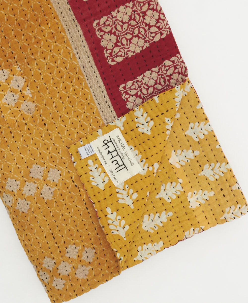 yellow-orange floral kantha quilt throw with a tag featuring the hand-stitched signature of the maker