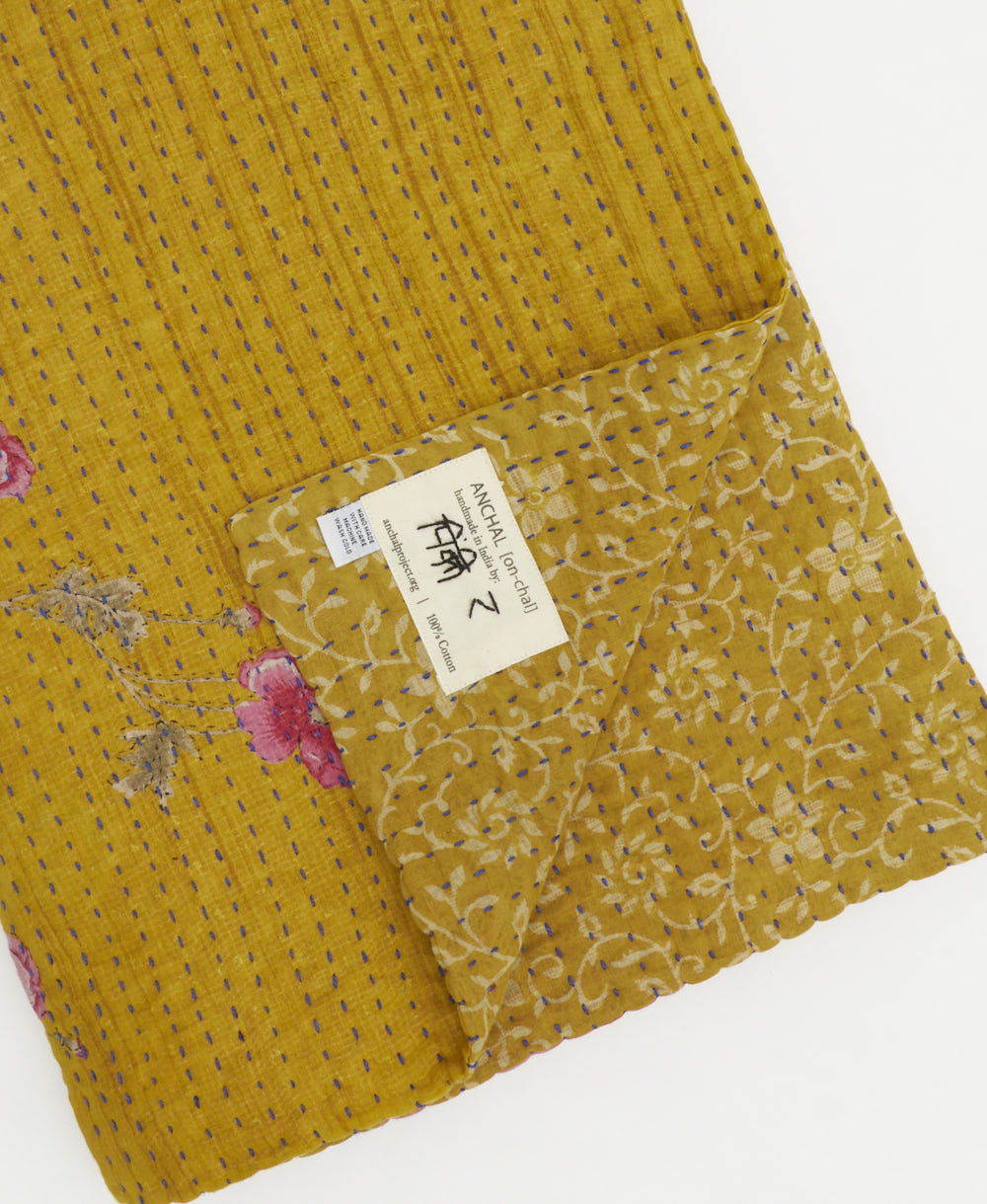kantha quilt throw with a tag featuring the hand-stitched signature of the maker