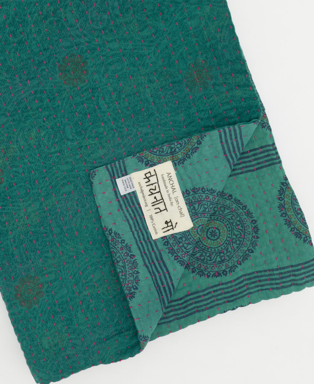 kantha quilt throw with a tag featuring the hand-stitched signature of the maker