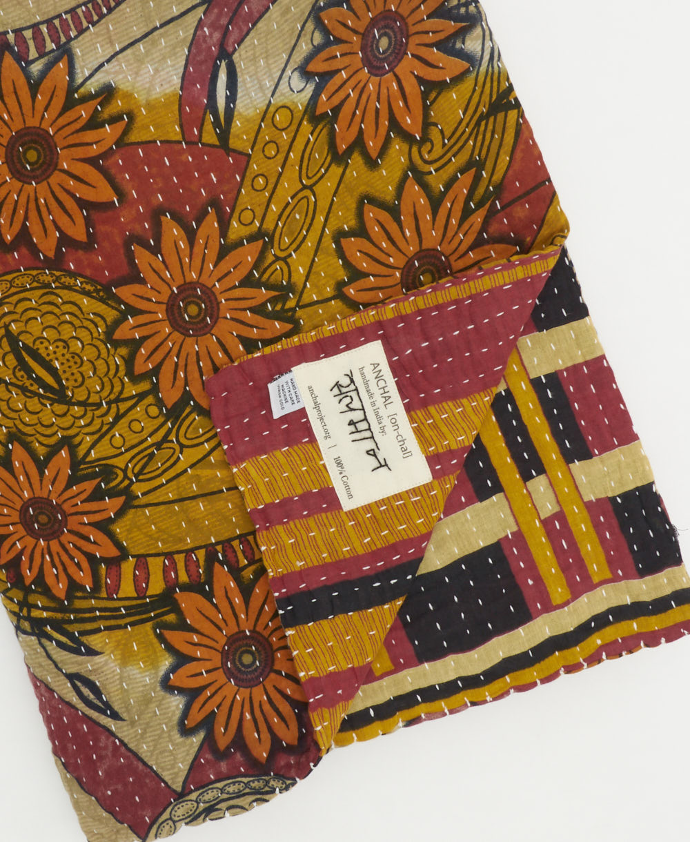 kantha quilt throw with a tag featuring the hand-stitched signature of the maker