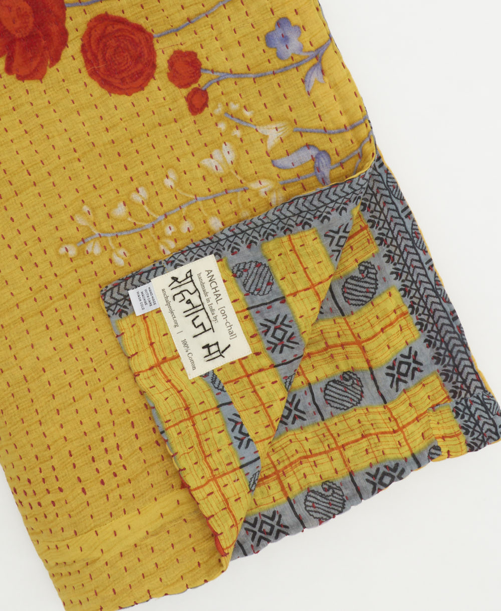 kantha quilt throw with a tag featuring the hand-stitched signature of the maker