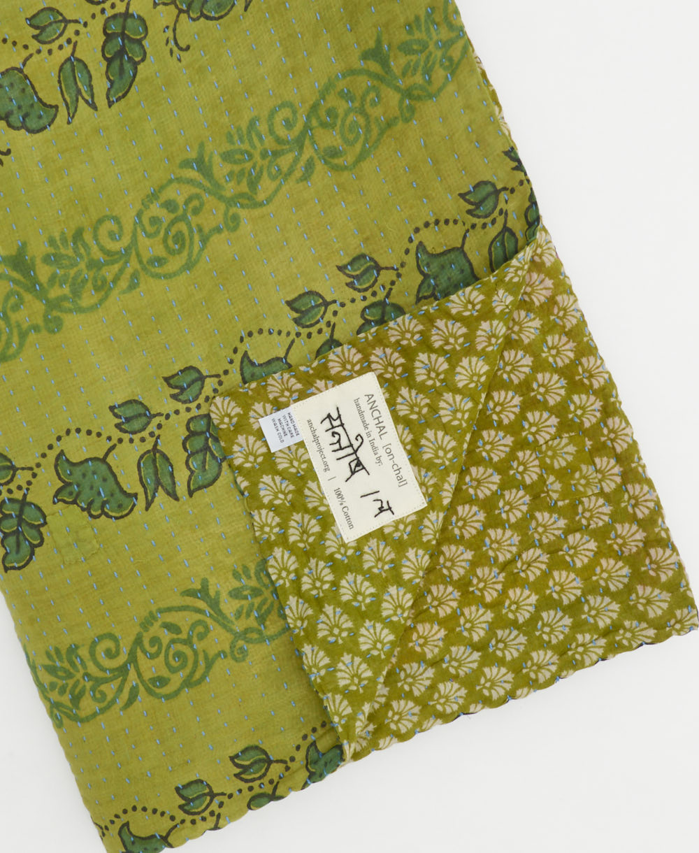 kantha quilt throw with a tag featuring the hand-stitched signature of the maker