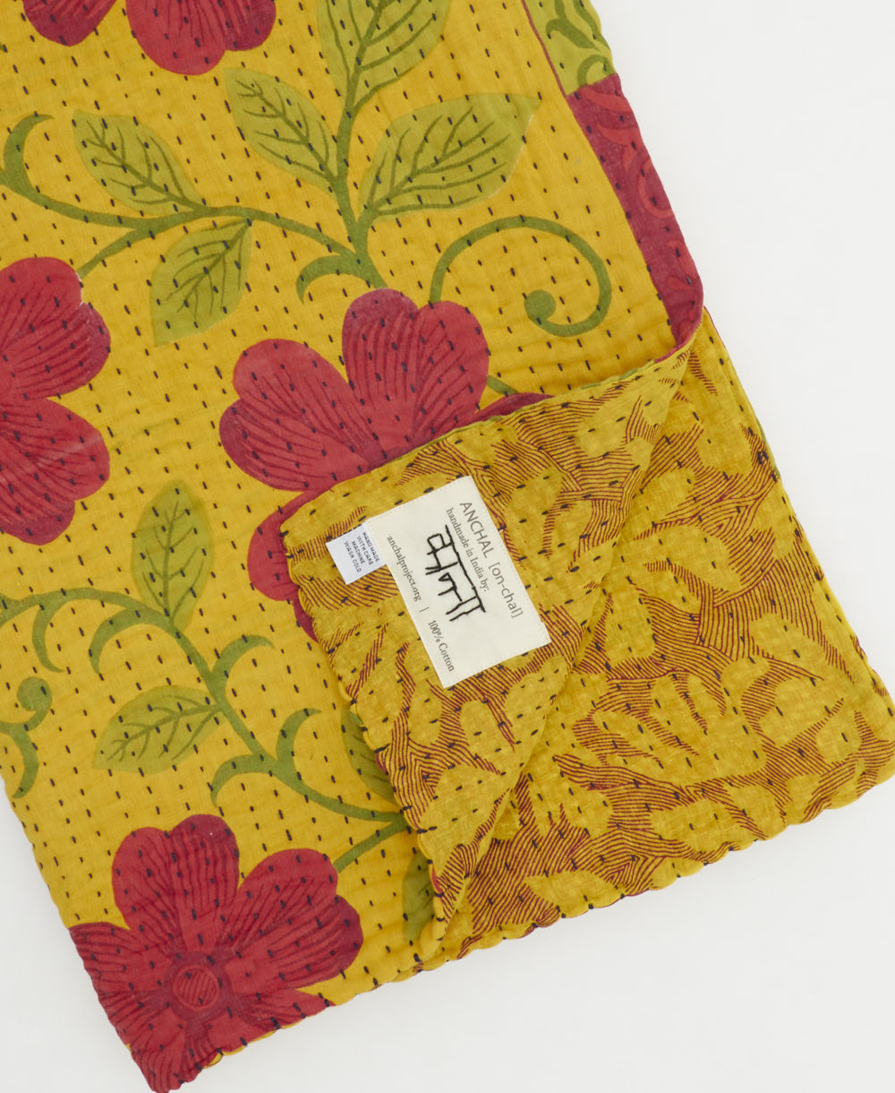 kantha quilt throw with a tag featuring the hand-stitched signature of the maker