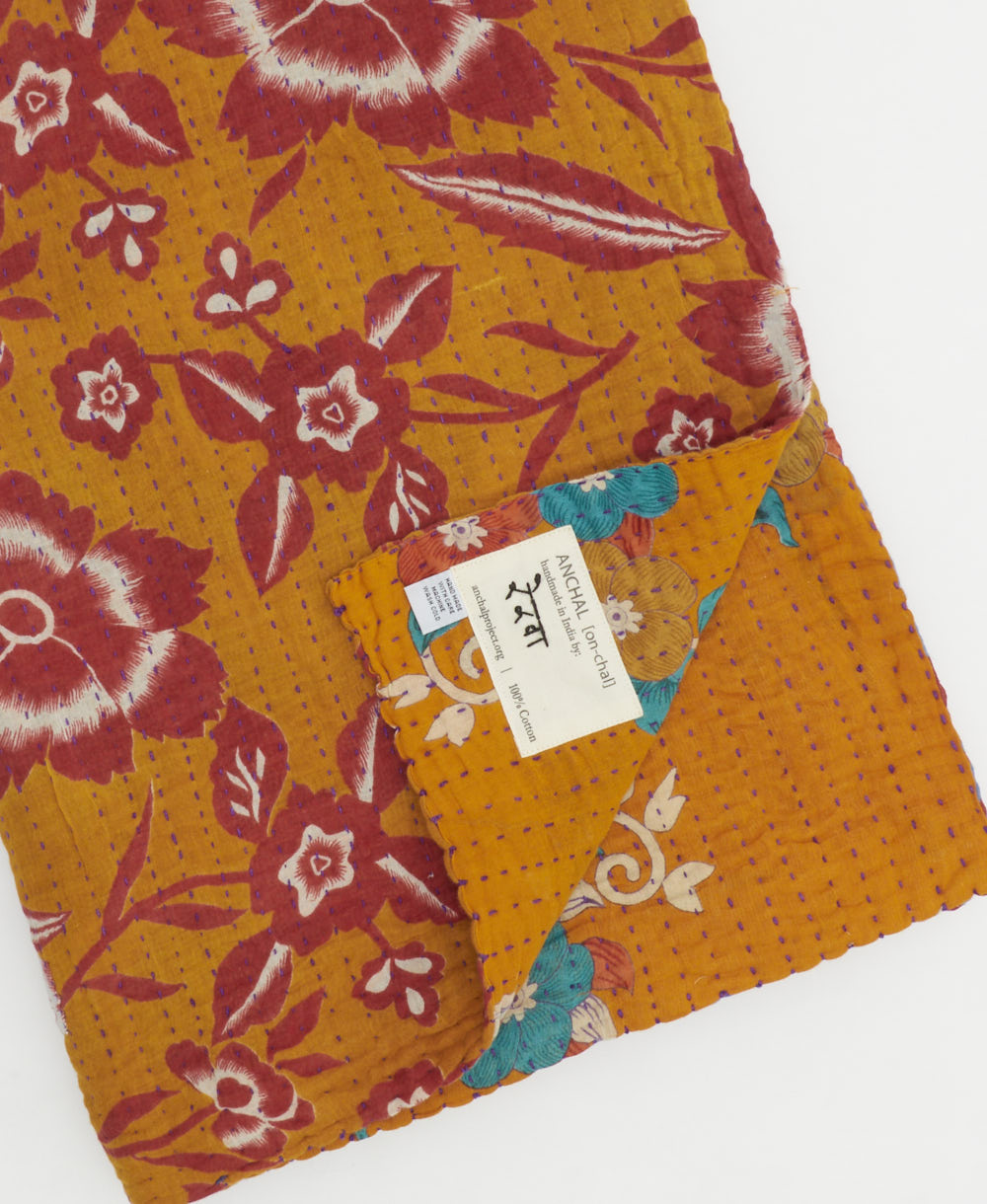 kantha quilt throw with a tag featuring the hand-stitched signature of the maker