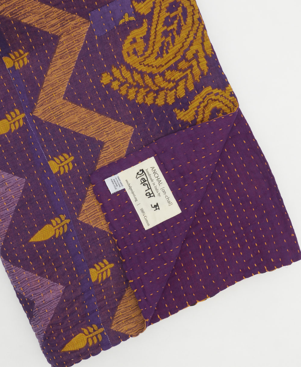 kantha quilt throw with a tag featuring the hand-stitched signature of the maker