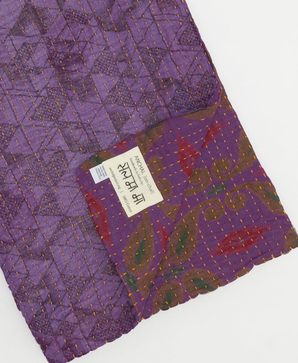 kantha quilt throw with a tag featuring the hand-stitched signature of the maker