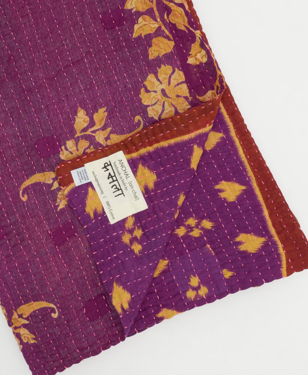 kantha quilt throw with a tag featuring the hand-stitched signature of the maker