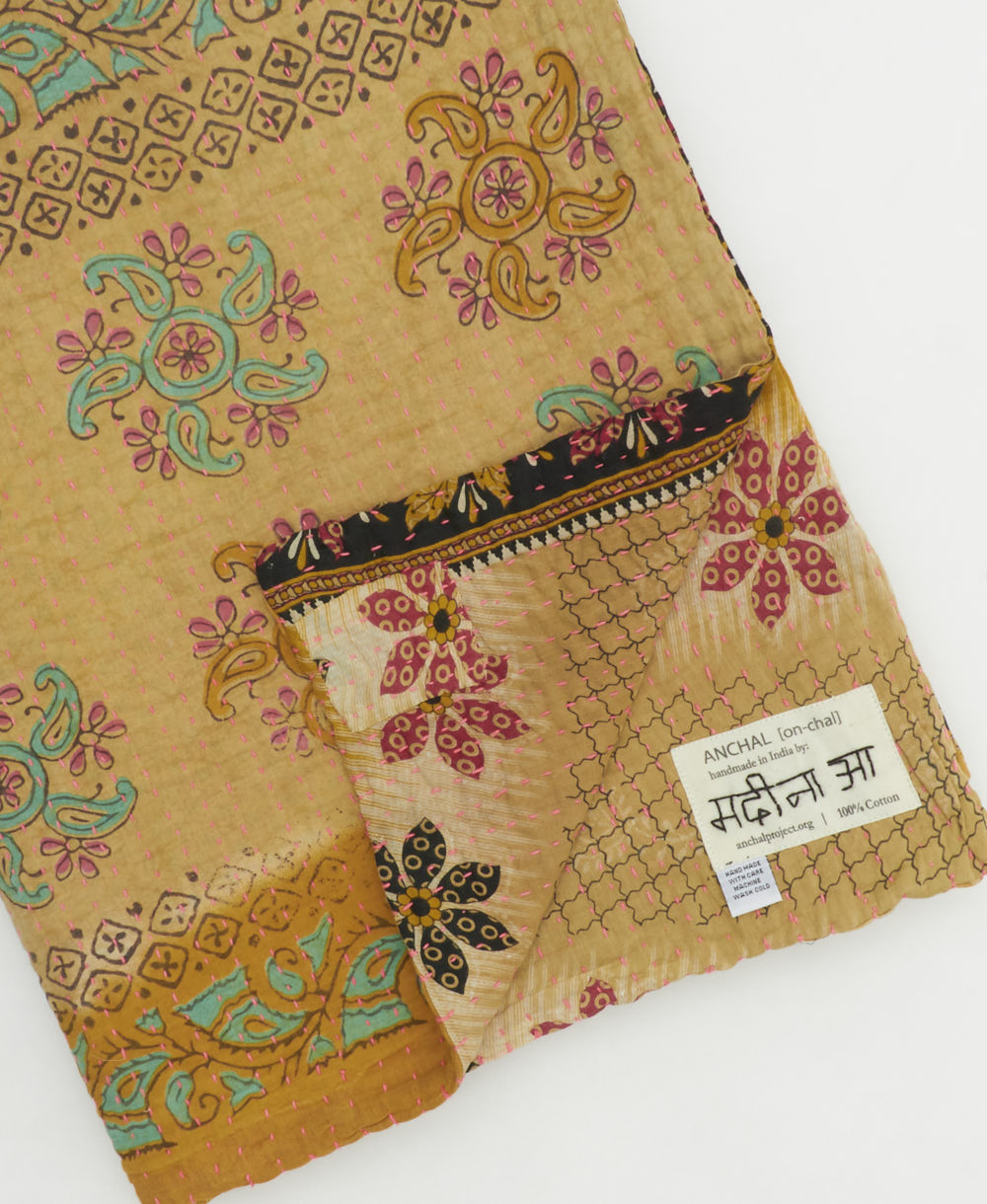 kantha quilt throw with a tag featuring the hand-stitched signature of the maker
