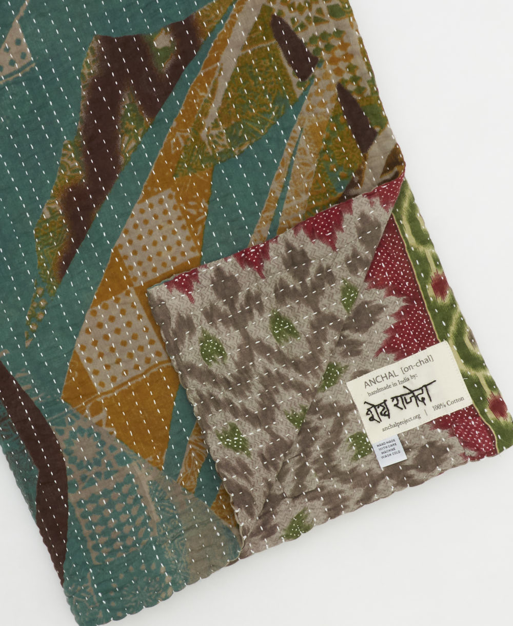 kantha quilt throw with a tag featuring the hand-stitched signature of the maker
