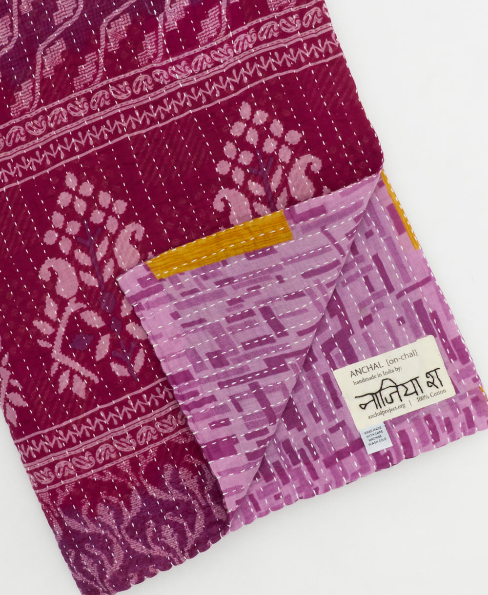 kantha quilt throw with a tag featuring the hand-stitched signature of the maker