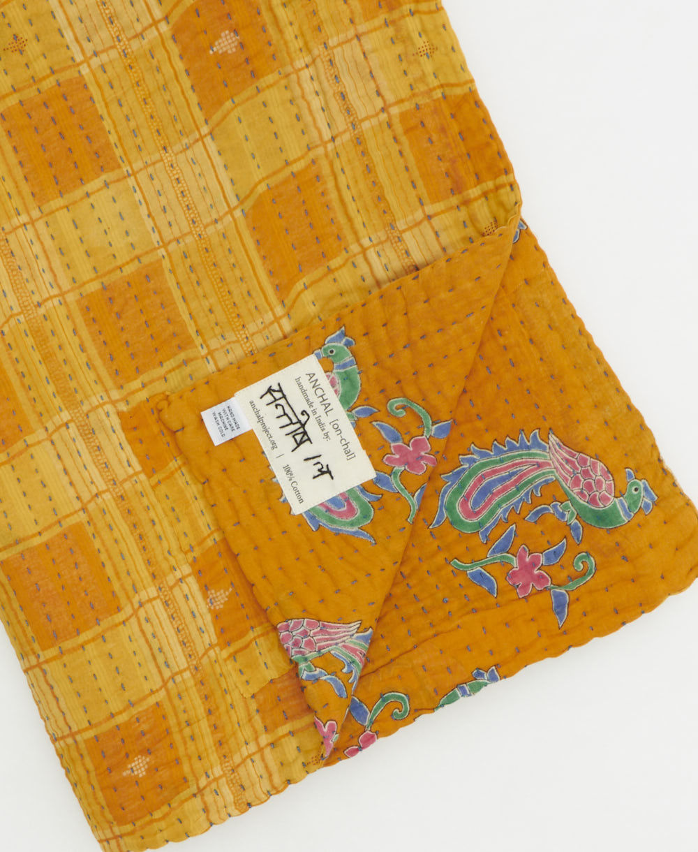 kantha quilt throw with a tag featuring the hand-stitched signature of the maker