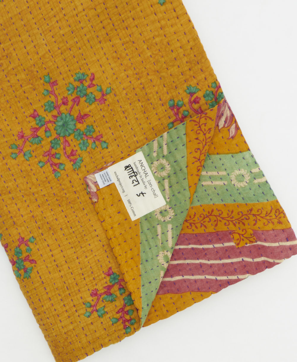 kantha quilt throw with a tag featuring the hand-stitched signature of the maker
