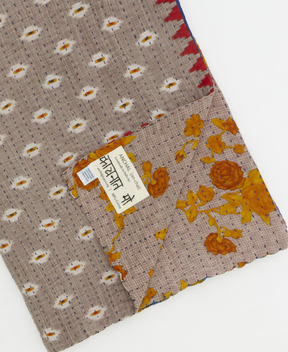 kantha quilt throw with a tag featuring the hand-stitched signature of the maker
