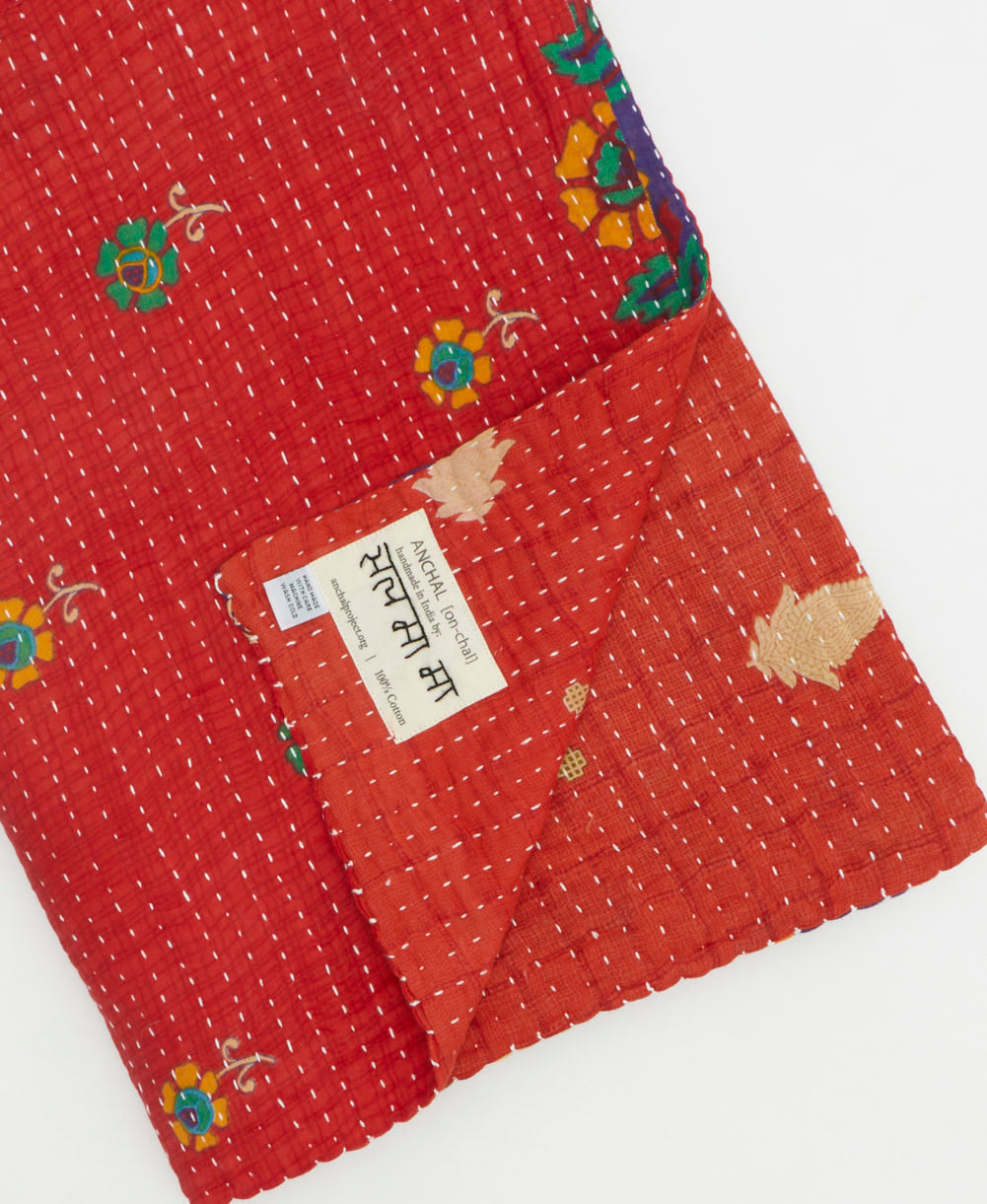 kantha quilt throw with a tag featuring the hand-stitched signature of the maker