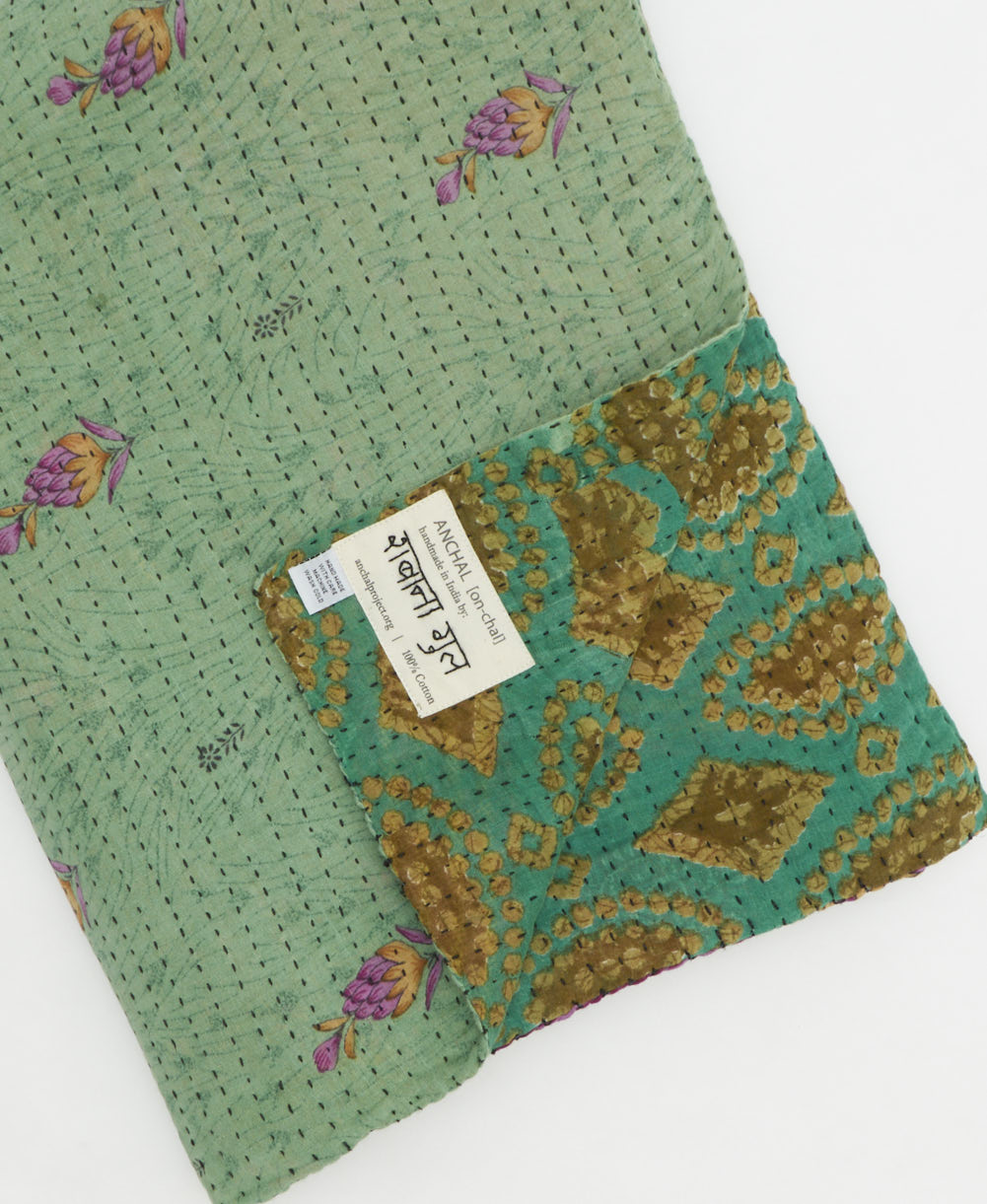 kantha quilt throw with a tag featuring the hand-stitched signature of the maker