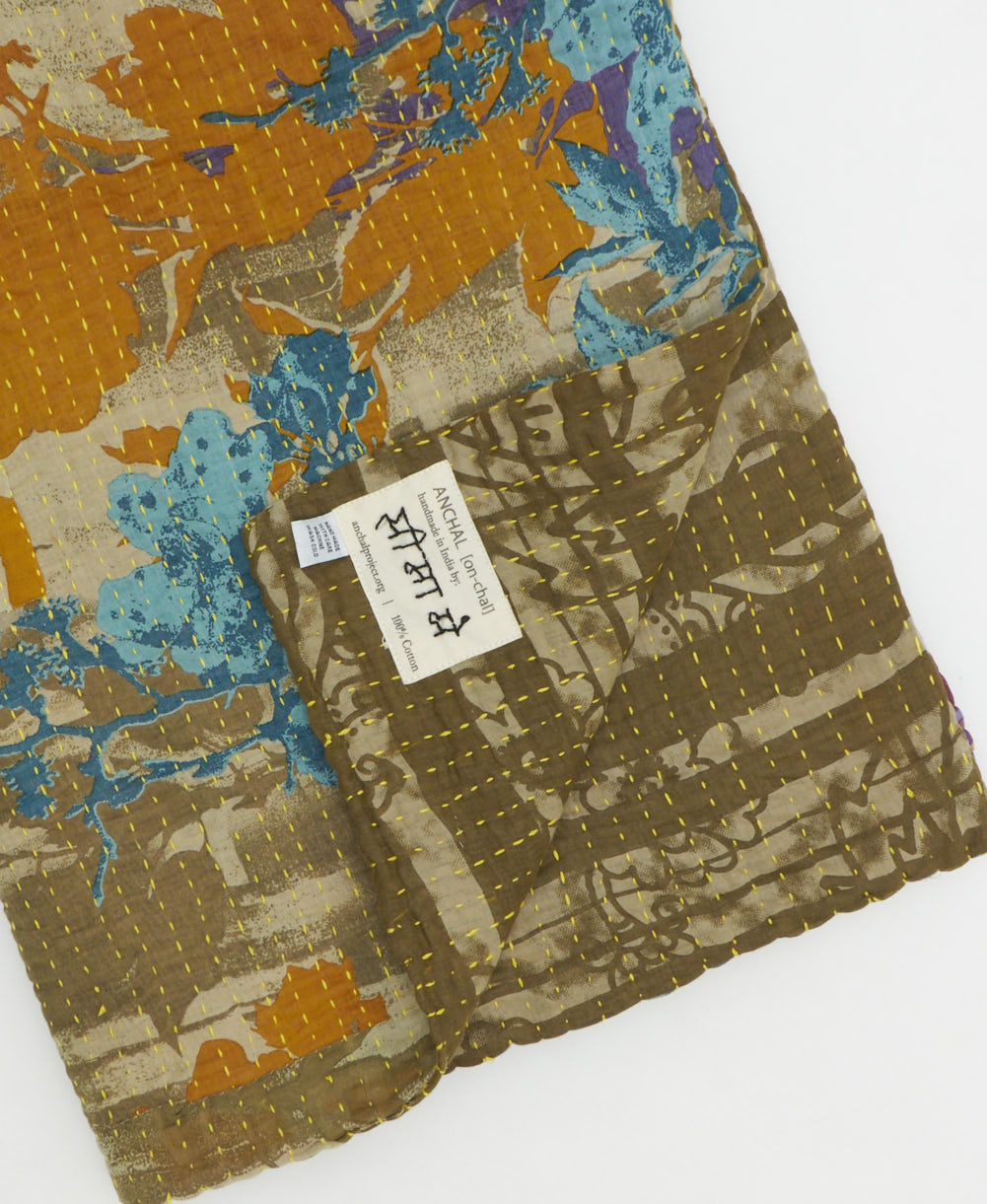 kantha quilt throw with a tag featuring the hand-stitched signature of the maker
