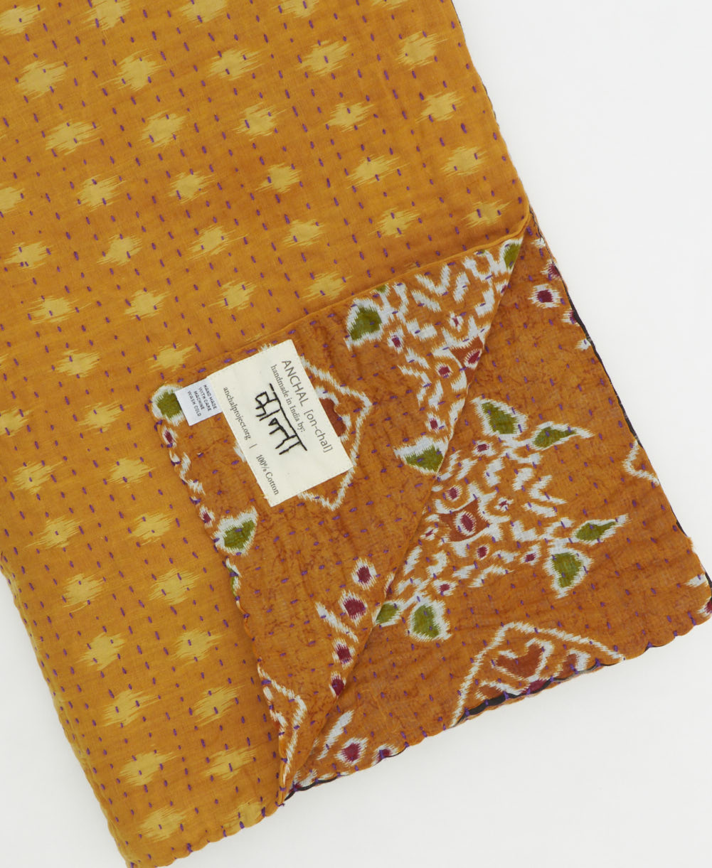 kantha quilt throw with a tag featuring the hand-stitched signature of the maker