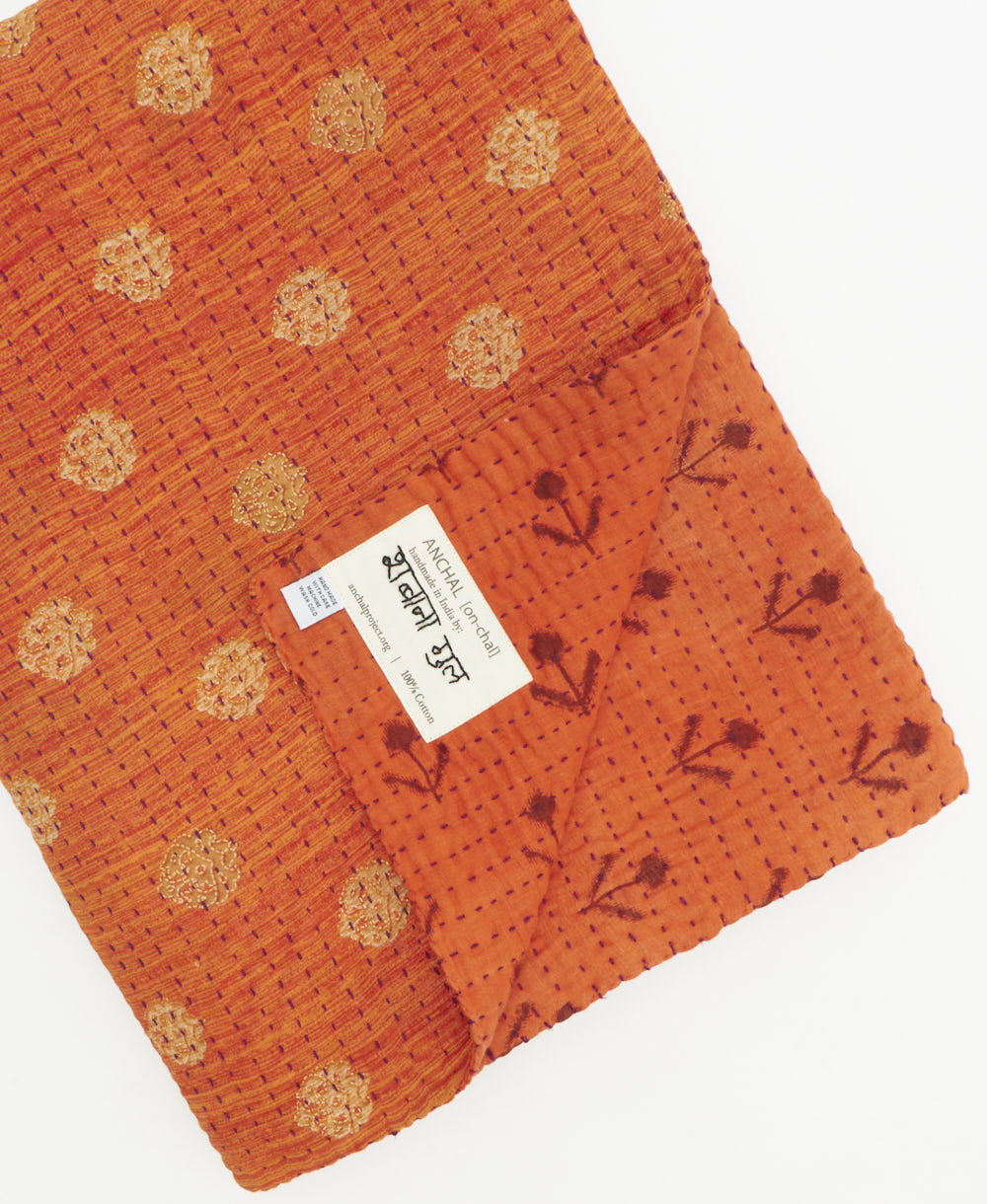 kantha quilt throw with a tag featuring the hand-stitched signature of the maker