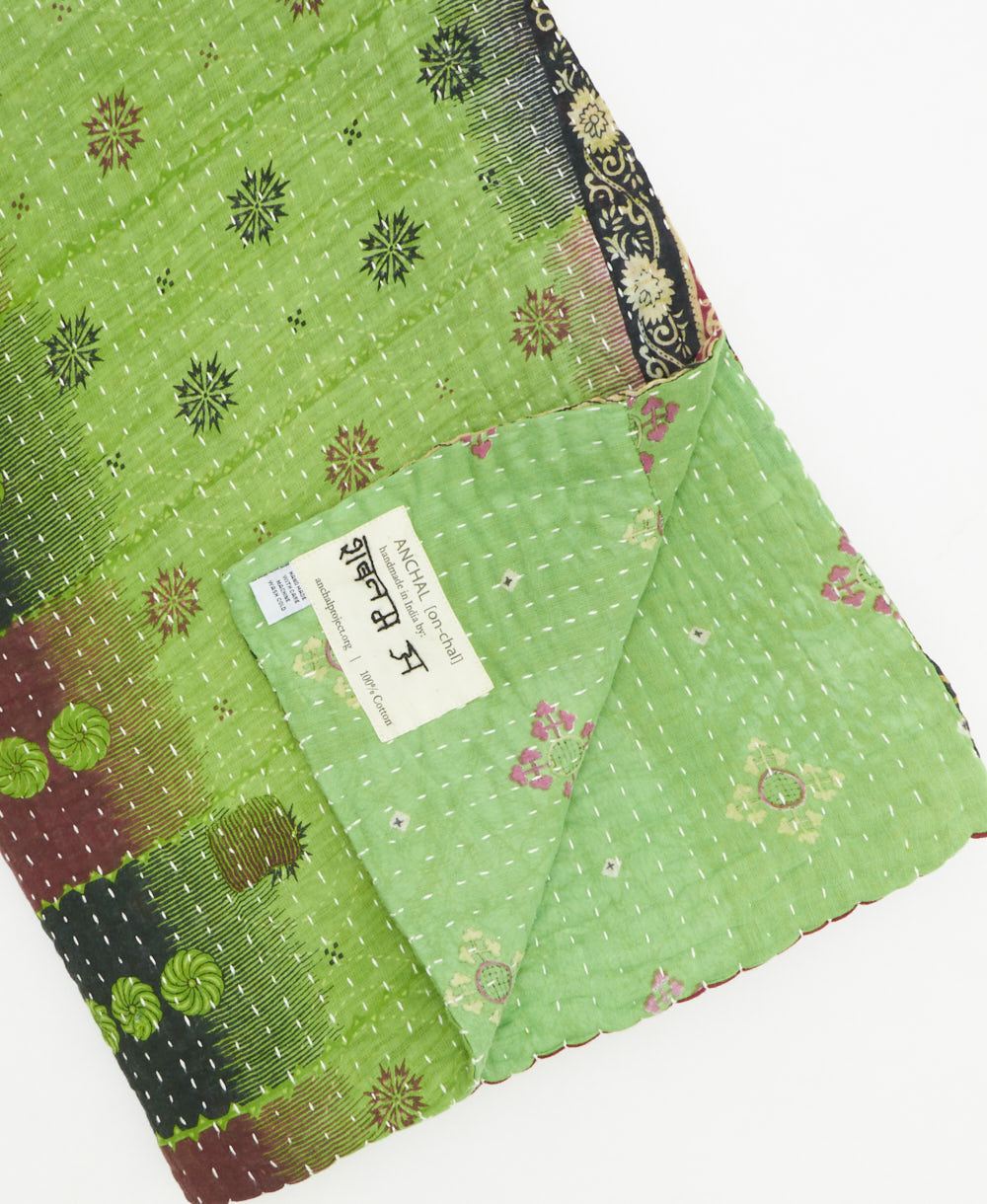 kantha quilt throw with a tag featuring the hand-stitched signature of the maker