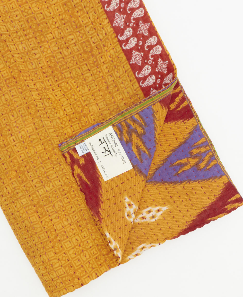 kantha quilt throw with a tag featuring the hand-stitched signature of the maker