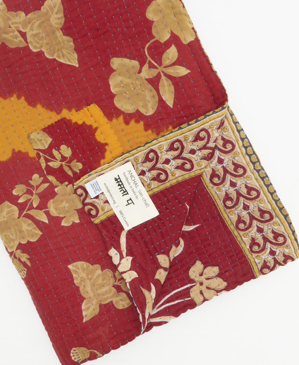 kantha quilt throw with a tag featuring the hand-stitched signature of the maker