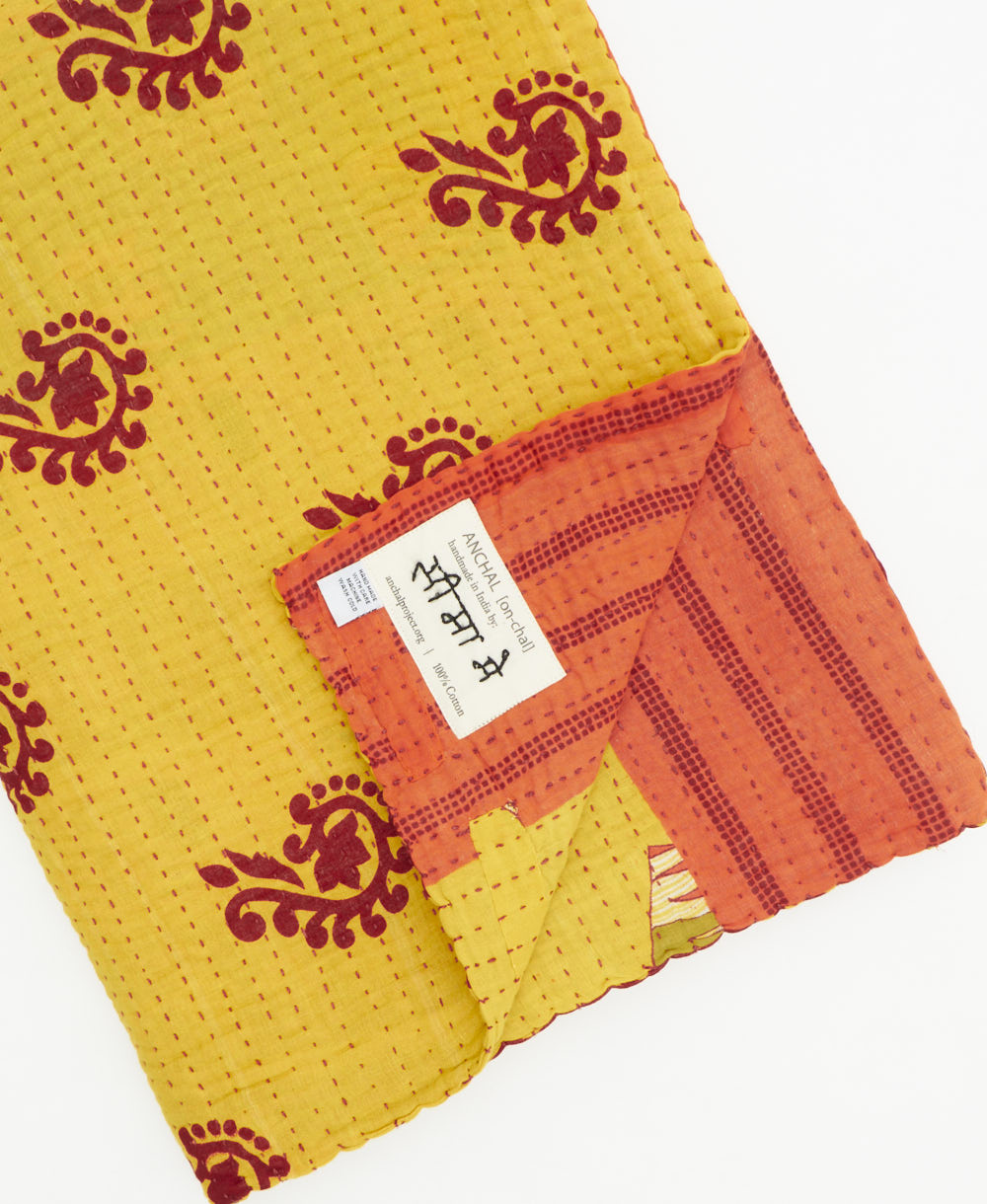 kantha quilt throw with a tag featuring the hand-stitched signature of the maker