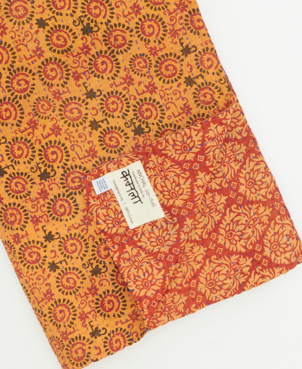 kantha quilt throw with a tag featuring the hand-stitched signature of the maker