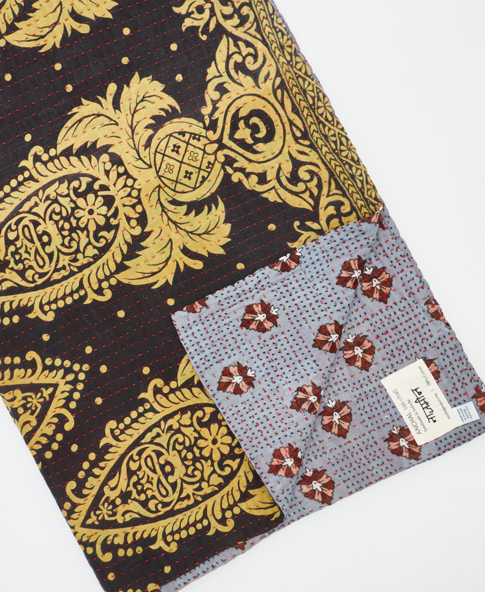 kantha quilt throw with a tag featuring the hand-stitched signature of the maker