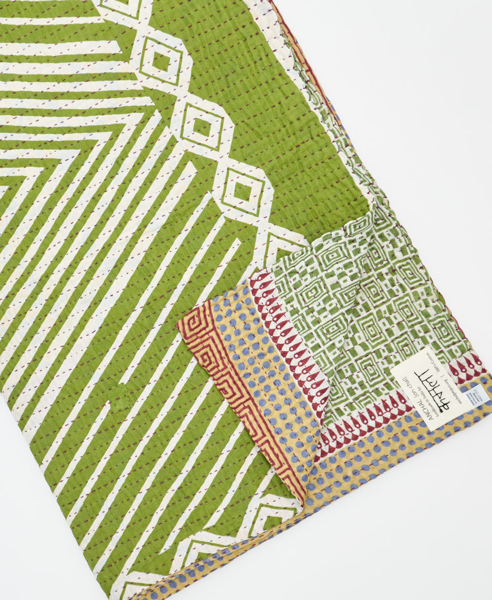 kantha quilt throw with a tag featuring the hand-stitched signature of the maker