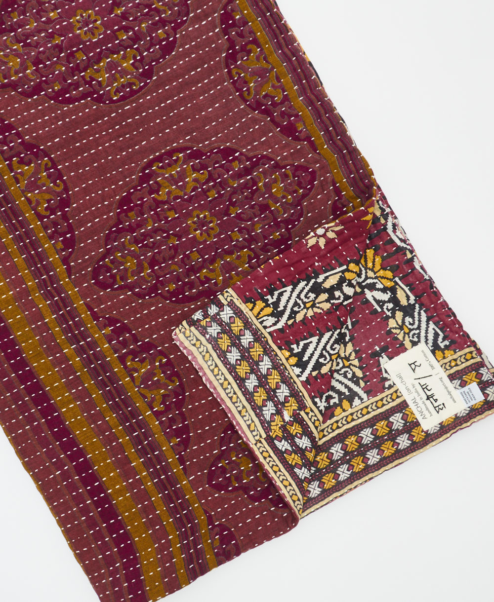 kantha quilt throw with a tag featuring the hand-stitched signature of the maker