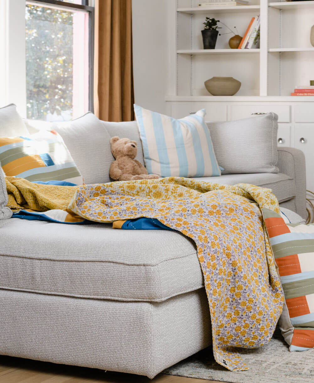 yellow floral kantha quilt draped over modern grey sofa with coordinating bright, colorful pillows