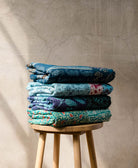 kantha quilts handmade in India in shades of blue folded on wooden stool