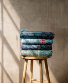 folded stack of unique blue kantha quilts each one-of-a-kind on light wooden stool