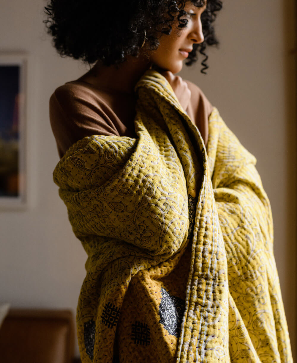 woman wrapped in canary yellow kantha quilt made from upcycled vintage saris in India by Anchal artisans