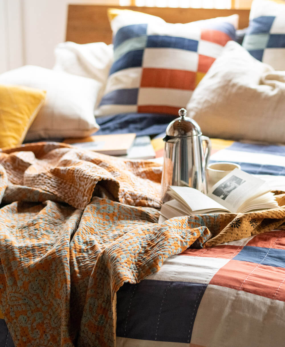 ethically made kantha blanket in orange paisley draped at the end of a colorful queen bed