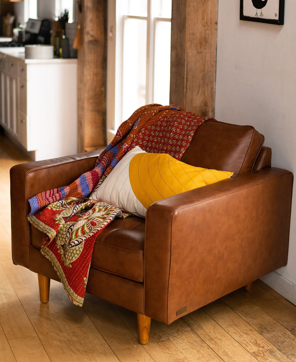 red kantha blanket draped over a chesnut brown modern armchair with modern yellow pillow