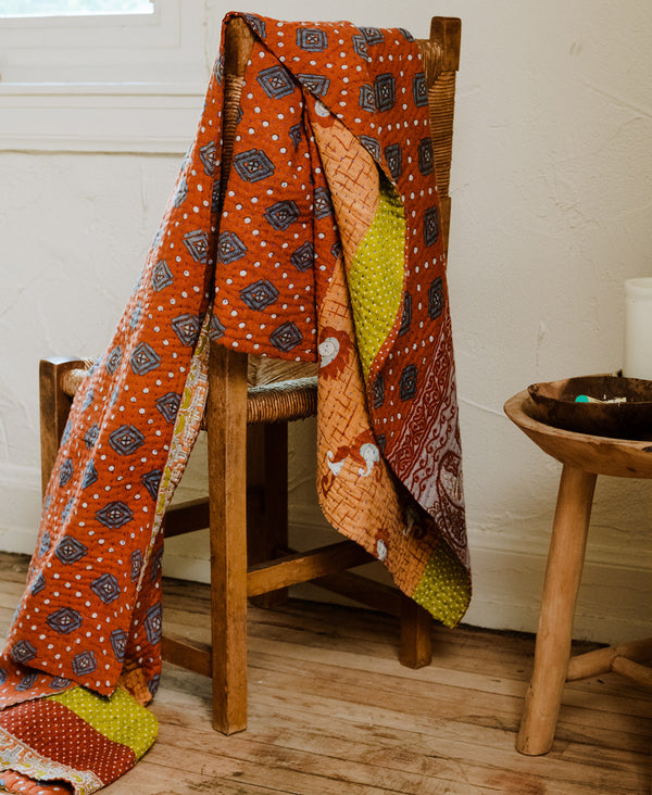 ethically made kantha quilt in warm tones draped over vintage wooden chair