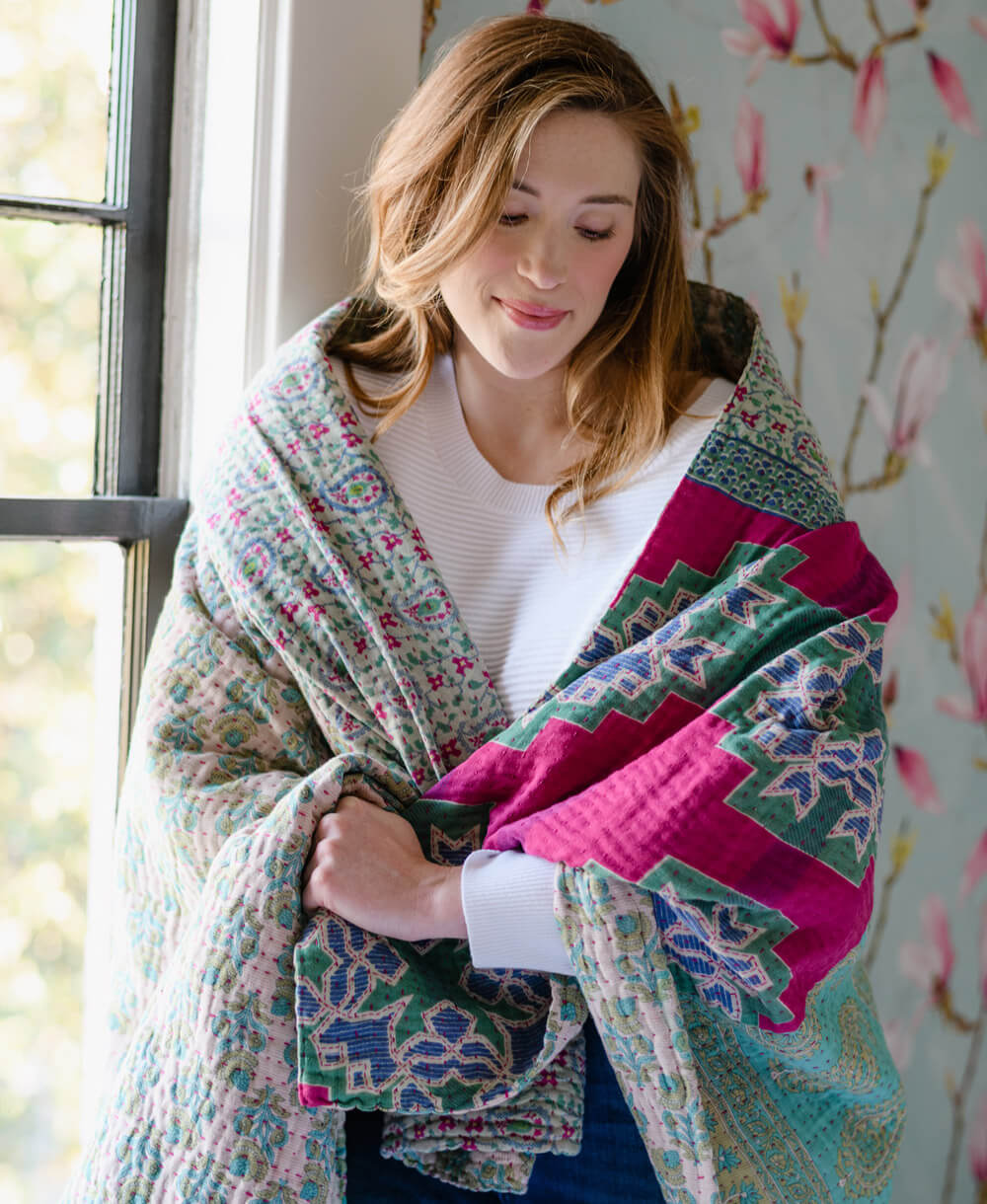 sky blue and hot pink kantha quilt draped around woman's shoulders